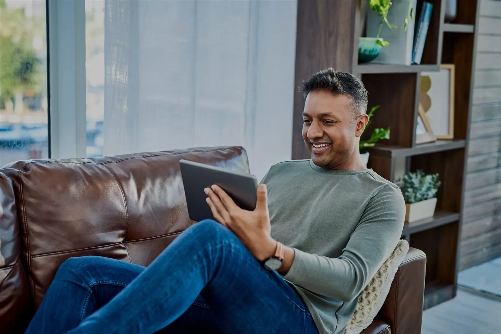 A clinician relaxes on a leather sofa, smiling at a tablet.