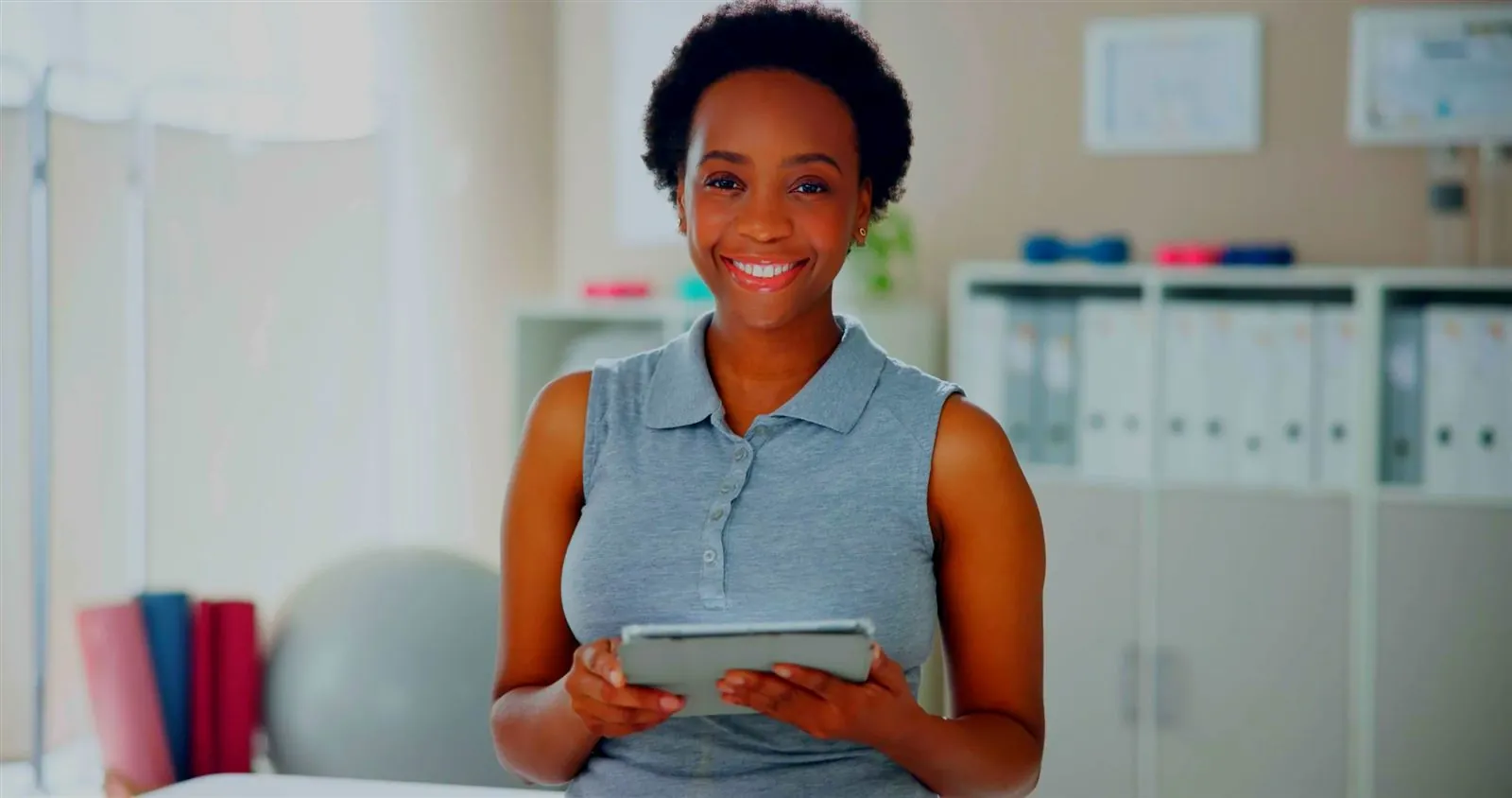 A clinician stands in an office holding a tablet, smiling.